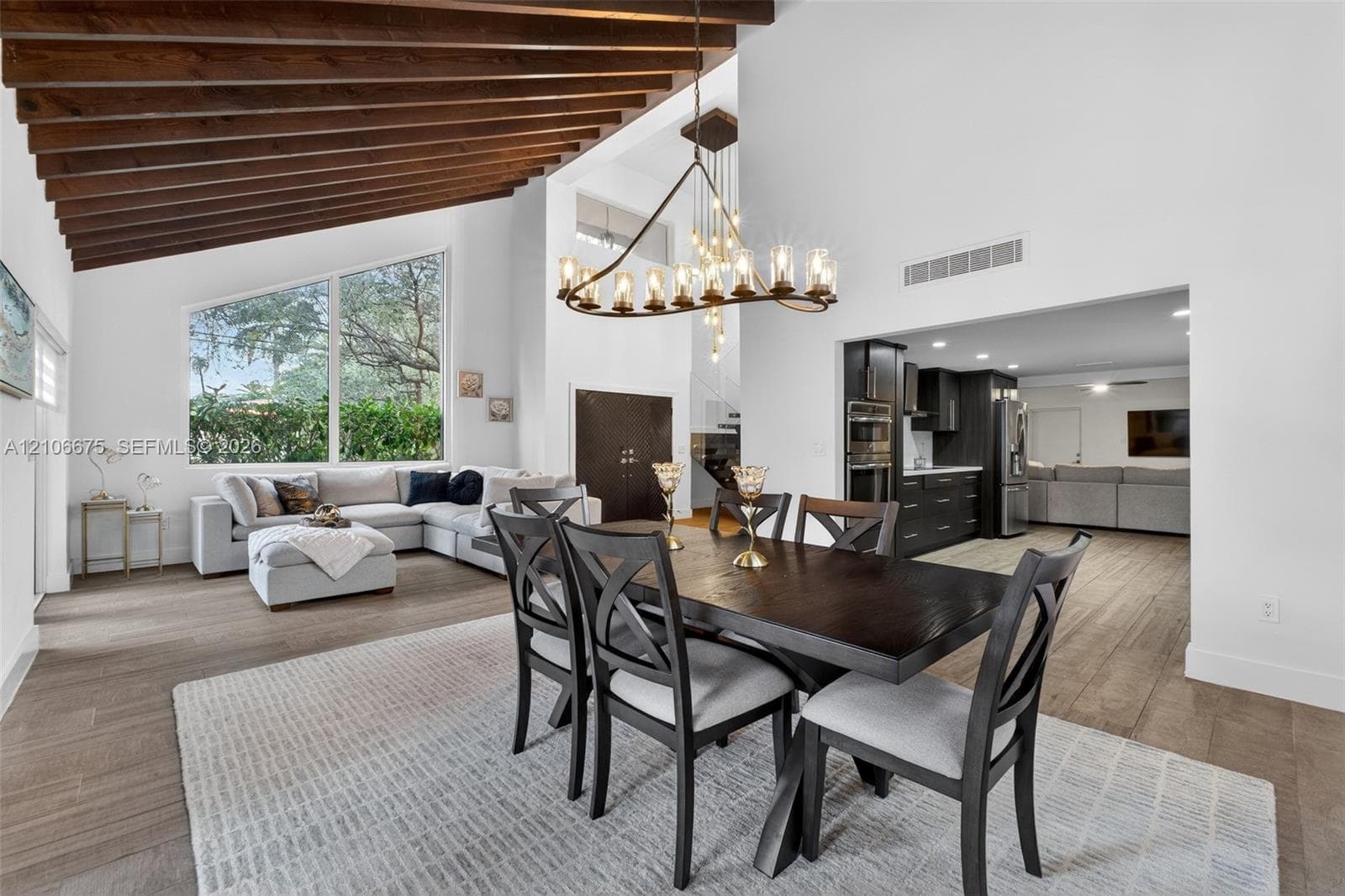 Vaulted ceiling with exposed wood beams, oversized picture window, wood-finish tile flooring, and multi-light industrial-style chandelier