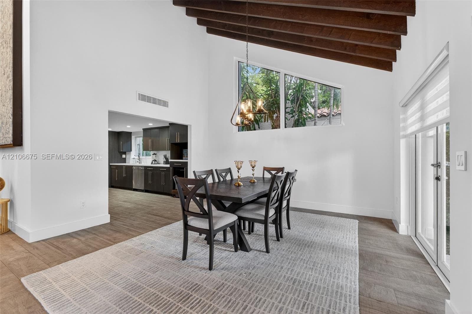 Vaulted ceilings featuring exposed wood beams, wood-finish flooring, geometric accent window, and double glass sliding doors