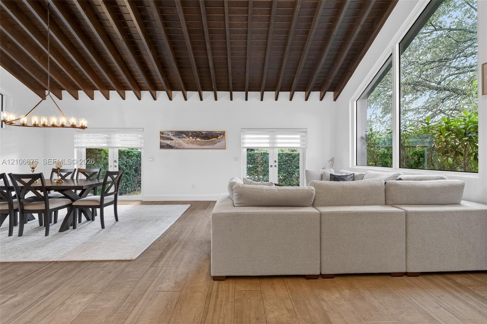 Vaulted ceiling with exposed wooden beams, wood-finish flooring, floor-to-ceiling windows, and dual sets of glass doors