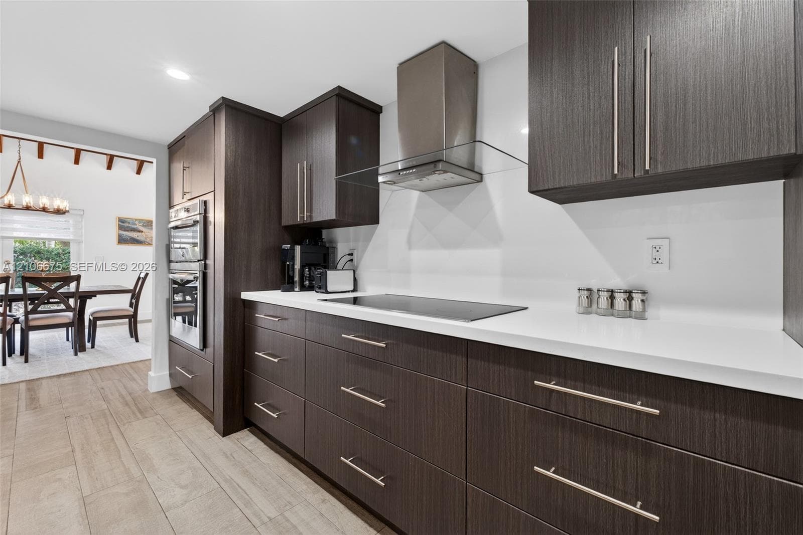 Kitchen featuring dark wood-finish cabinetry, solid surface countertops, a glass and stainless steel range hood, integrated cooktop, and built-in wall oven