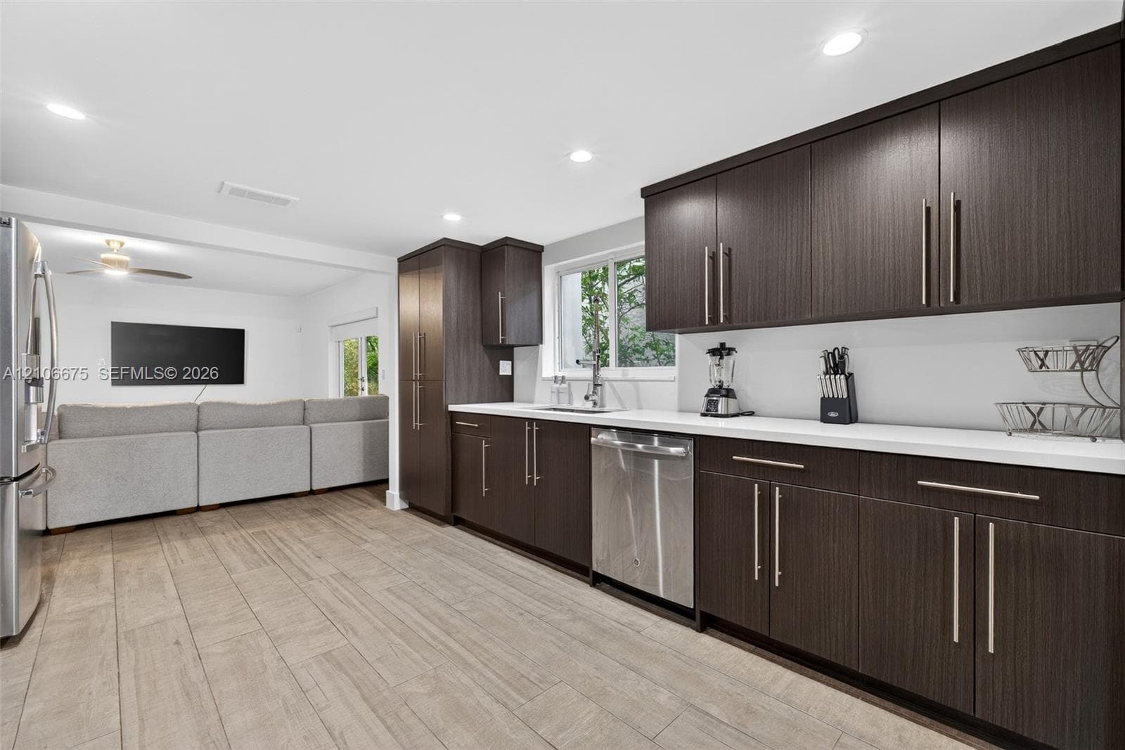 Kitchen featuring dark-toned cabinetry, stainless steel appliances, white solid-surface countertops, and wood-finish flooring