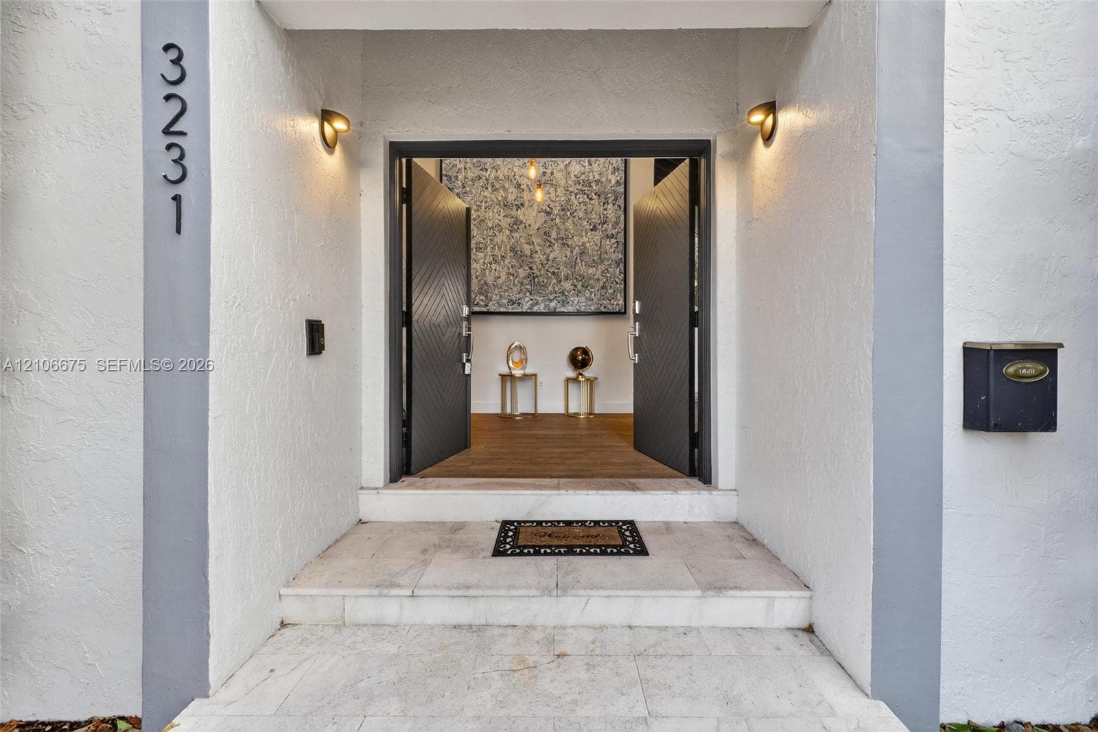 Entryway featuring double-door entrance with chevron-pattern detailing, stone-tiled steps, wall-mounted light fixtures, and exterior building number signage
