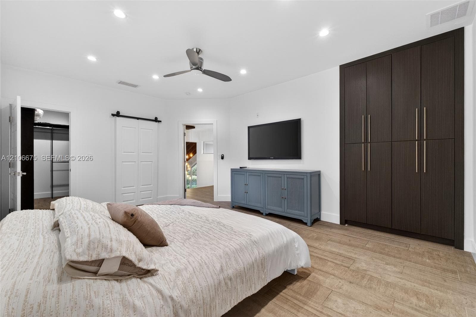 Spacious interior featuring wood-finish flooring, recessed lighting, ceiling fan, floor-to-ceiling built-in dark cabinetry, and white sliding barn door