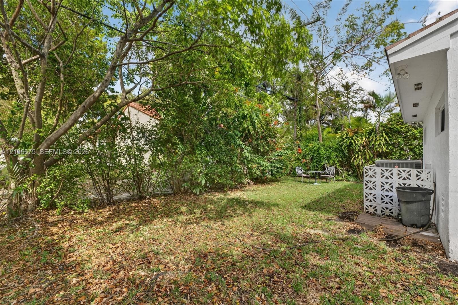Outdoor space featuring a grass yard, mature trees, dense perimeter vegetation, and decorative concrete masonry privacy screen