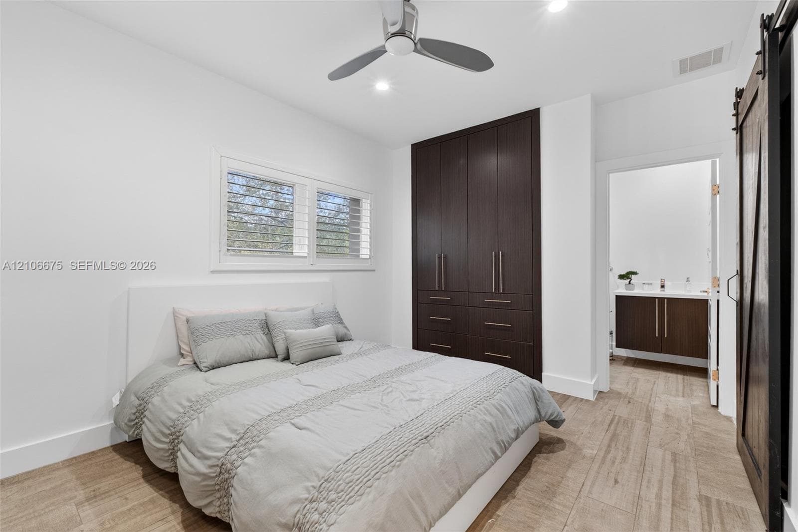 Wood-finish flooring, custom floor-to-ceiling dark cabinetry, window shutters, sliding barn door, and a three-blade ceiling fan