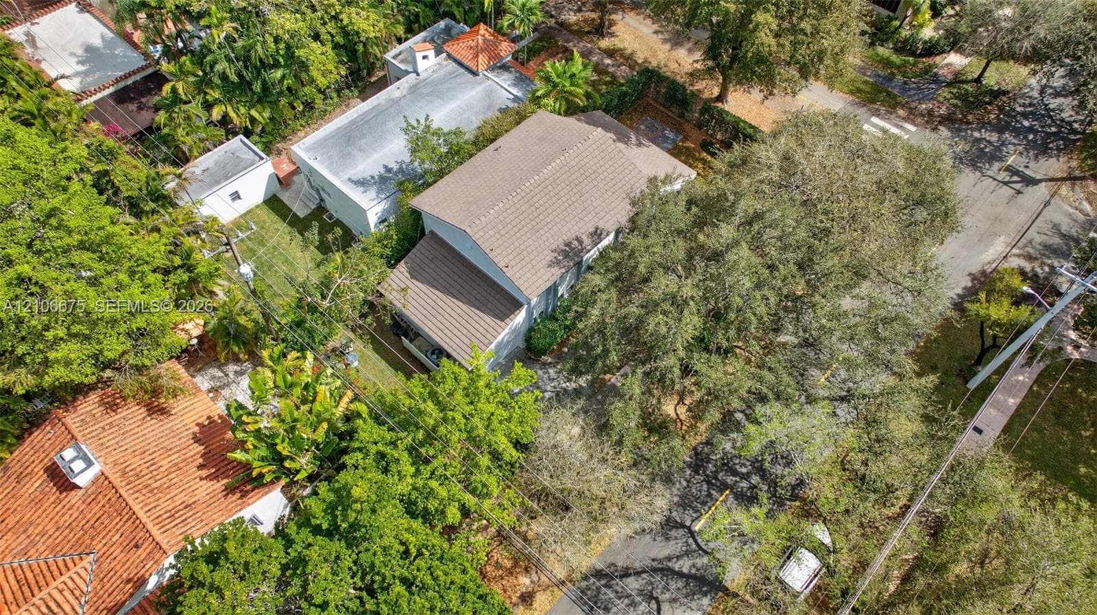 Aerial perspective of a multi-level structure featuring a tile roof, paved driveway, and mature landscaping with extensive tree canopy coverage