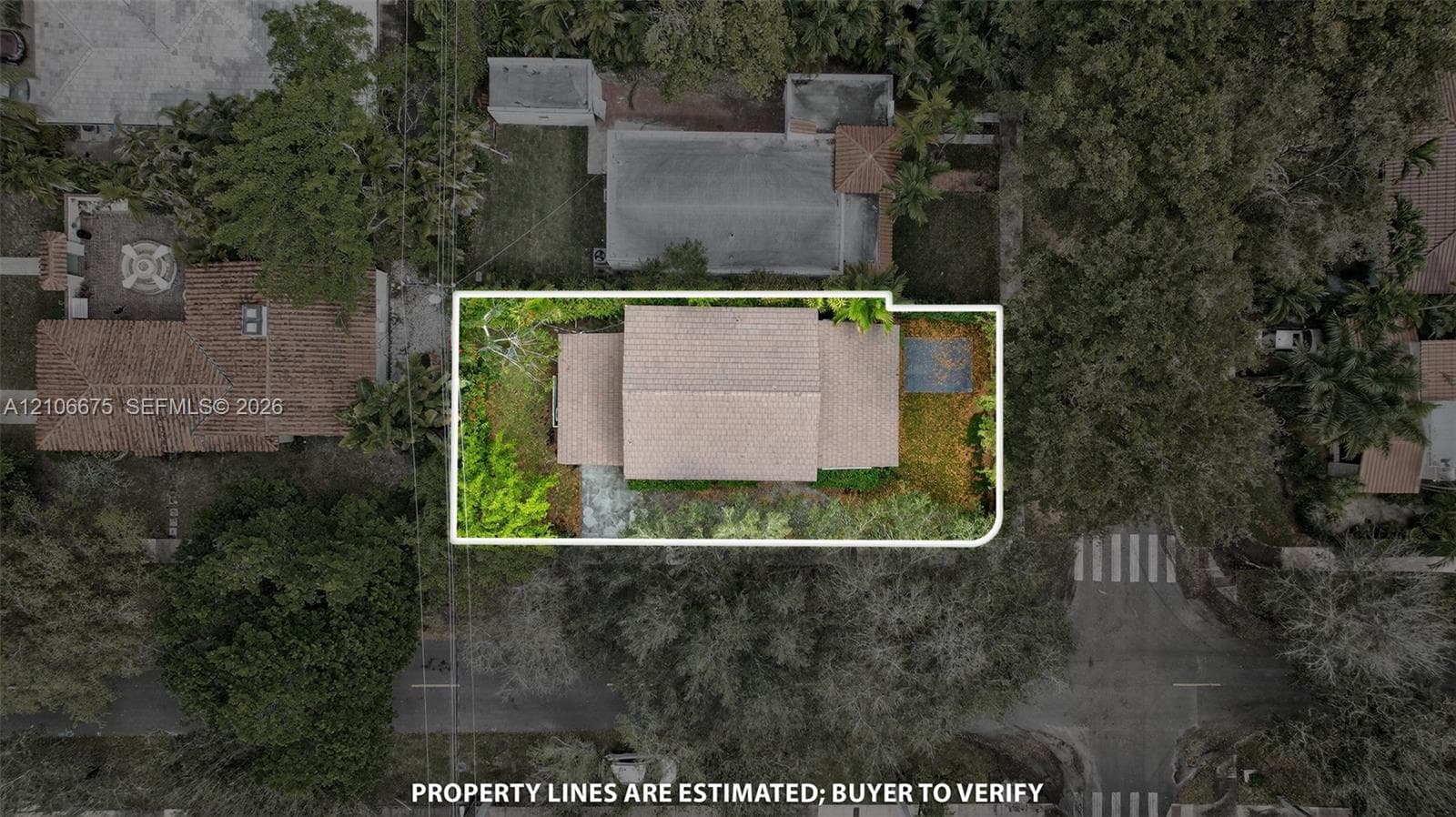 Aerial view of the property lot featuring mature trees, landscaped grounds, a shingled roofline, and hardscaped walkways