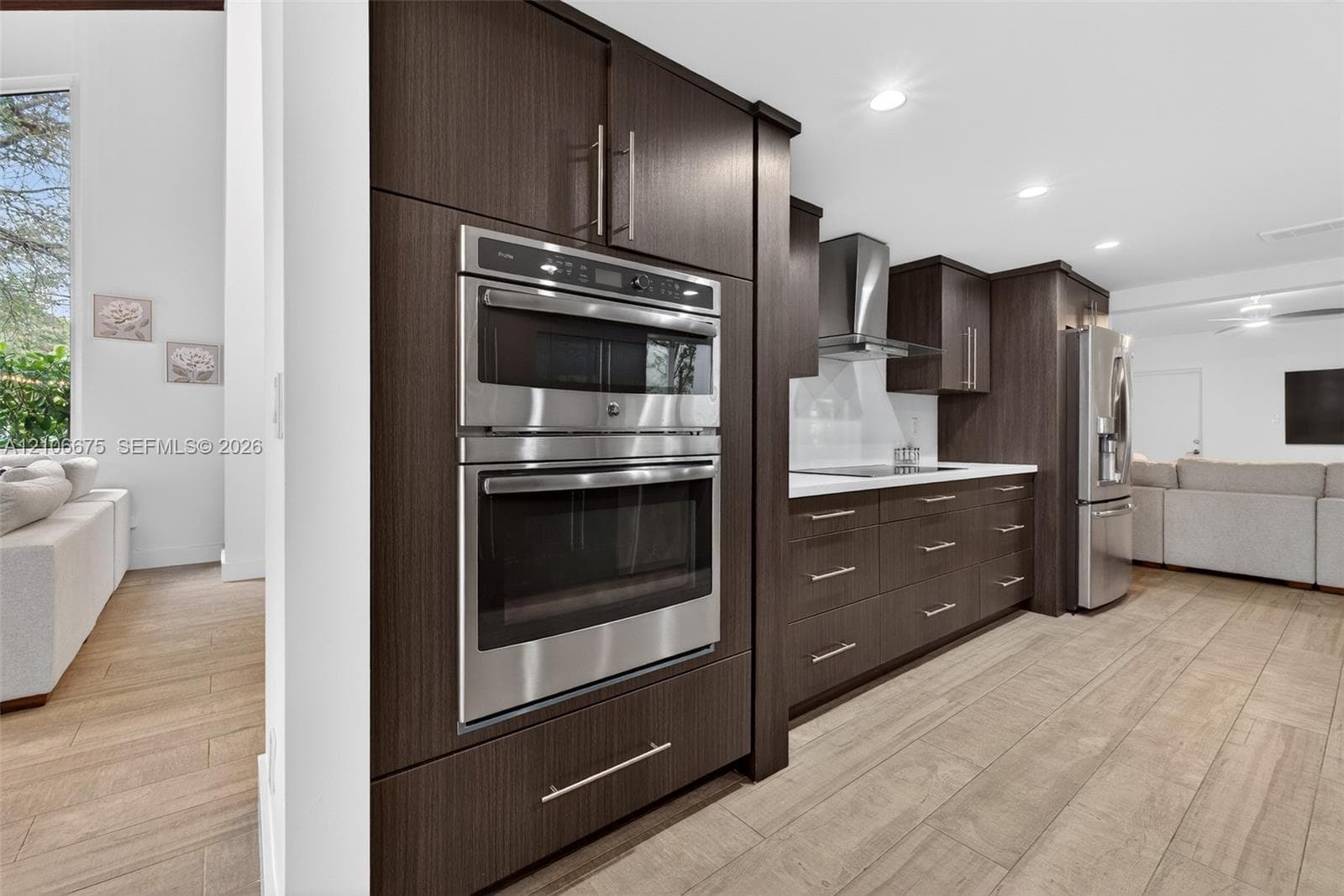 Custom dark wood-finish cabinetry, built-in stainless steel wall oven and microwave, stainless steel range hood, stone countertops, and wood-finish flooring