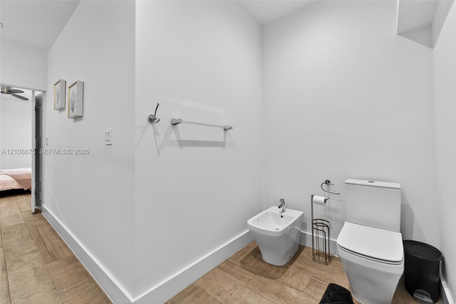 Restroom featuring wood-finish flooring, a wall-mounted metal towel bar, a white ceramic bidet with a chrome faucet, and a dual-flush toilet