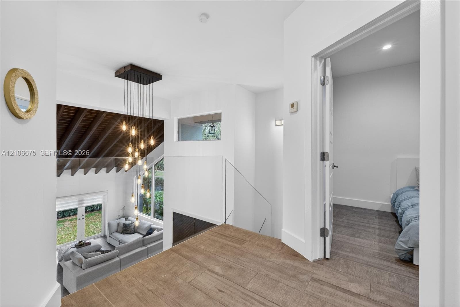 Open-plan interior featuring wood-finish flooring, a multi-pendant chandelier, a vaulted ceiling with exposed structural beams, and a glass-panel railing