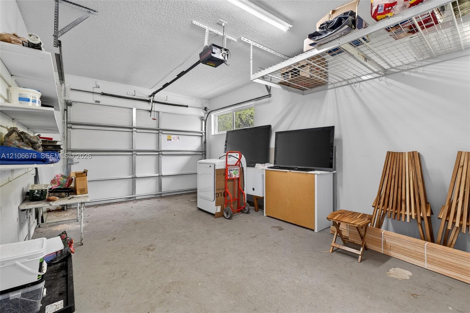 Garage interior featuring a sectional roll-up door, integrated ceiling-mounted shelving, built-in wall shelving, and linear overhead lighting
