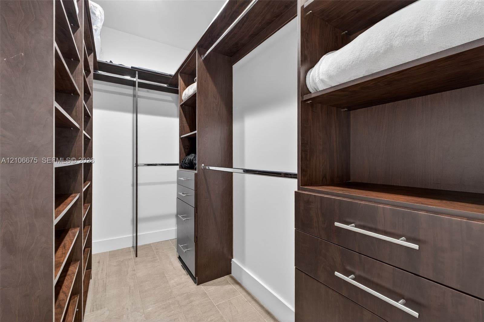 Walk-in closet featuring custom wood-finish cabinetry, built-in shelving, integrated dresser drawers with metallic hardware, and overhead hanging rods