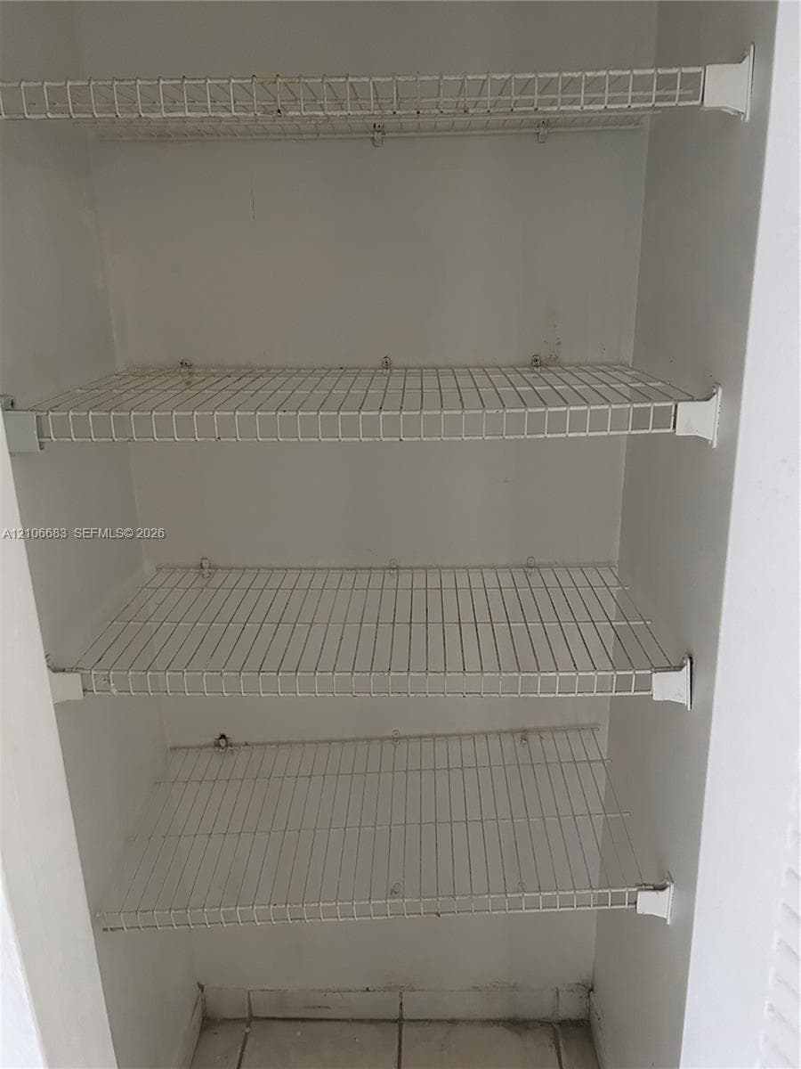 Storage closet featuring four tiers of white wire shelving and tiled flooring