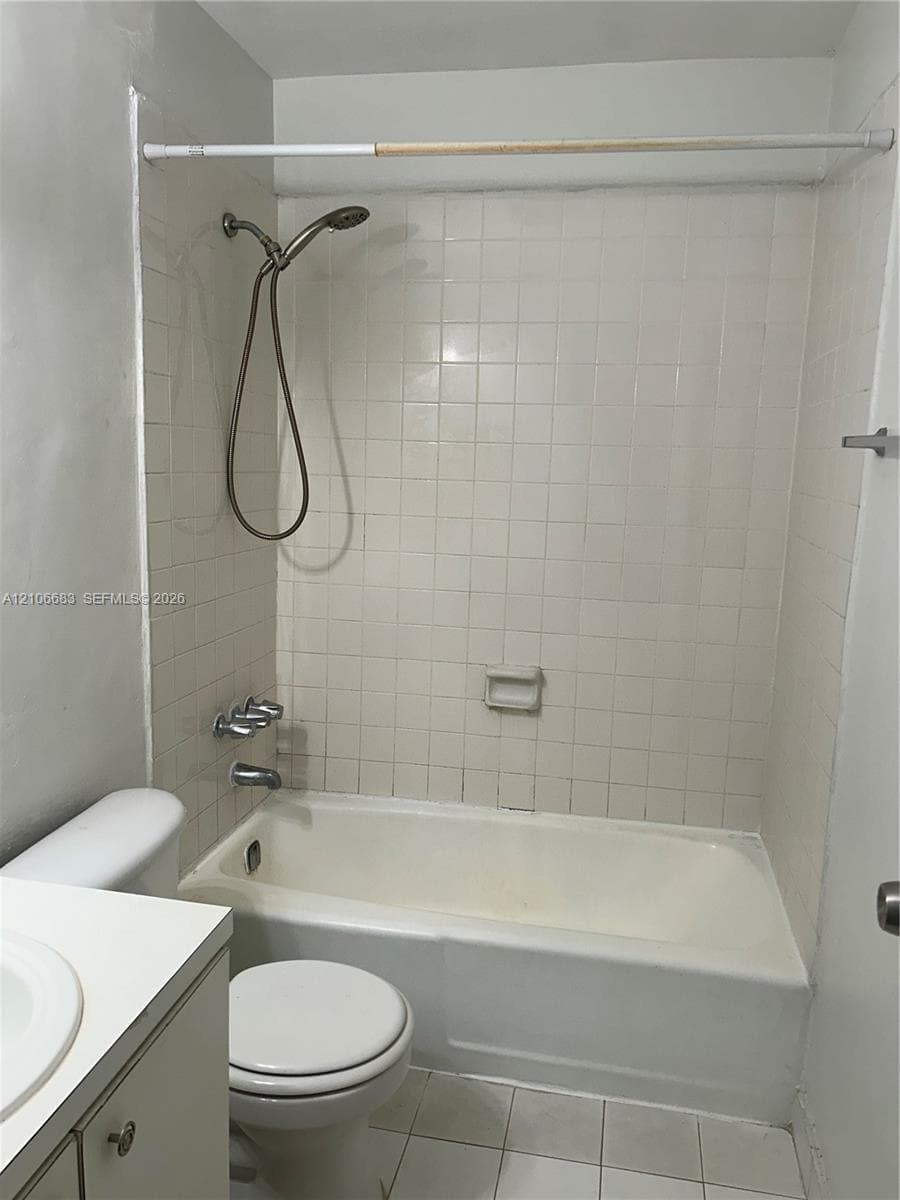Bathroom featuring a tiled tub-shower surround, adjustable handheld shower head, inset soap dish, and porcelain toilet