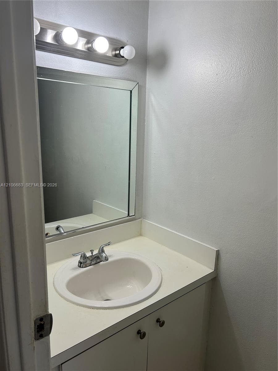 Vanity featuring an integrated sink, solid-surface countertop, cabinetry with round pulls, framed wall mirror, and a four-light fixture