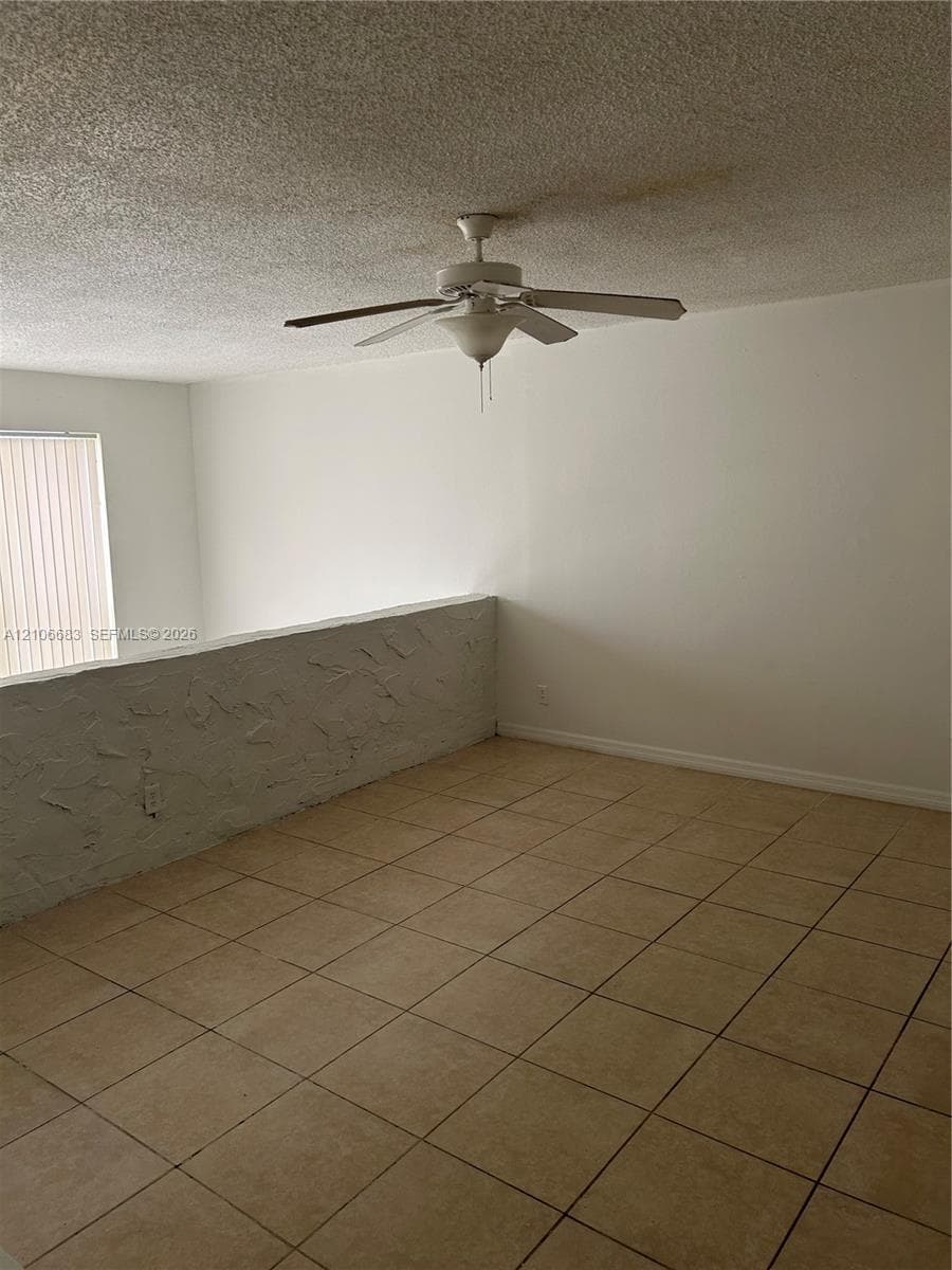 Ceramic tile flooring, textured wall accent, and ceiling fan with integrated light fixture