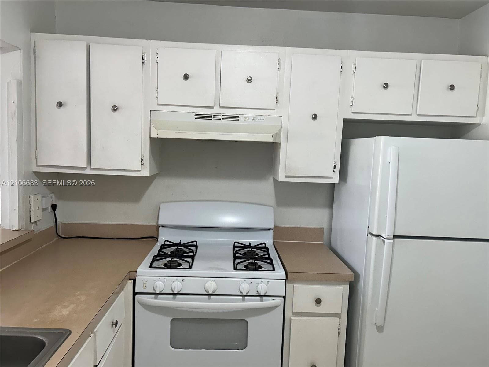 Kitchen featuring white cabinetry with circular hardware, neutral-toned countertops, a white gas range with an integrated hood, and a full-size white refrigerator