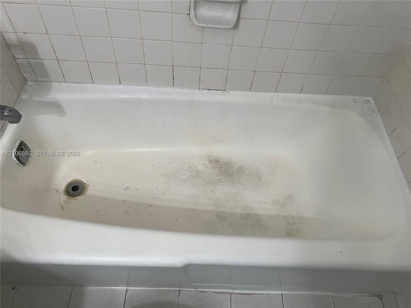 Bathtub with white square wall tile surround, integrated soap dish, and chrome-finish plumbing fixtures