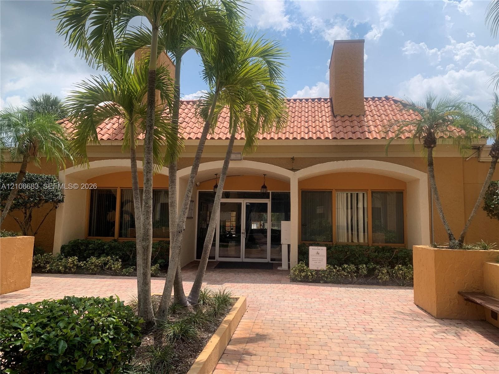 Exterior facade featuring stucco siding, a terracotta tile roof, arched architectural details, and a paved brick courtyard