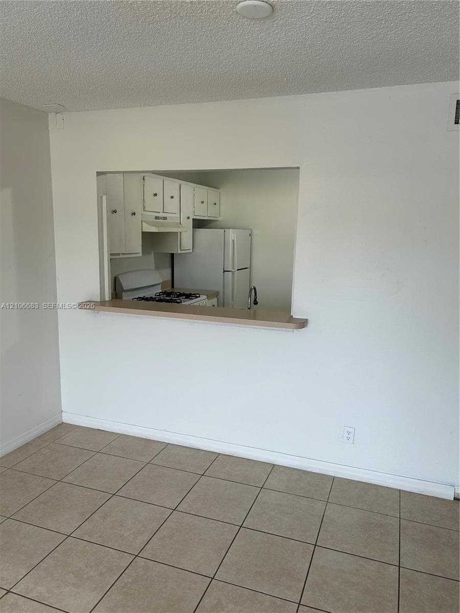 Kitchen features an open pass-through window with a built-in counter, white cabinetry, a white refrigerator, and a gas range, all finished with ceramic tile flooring