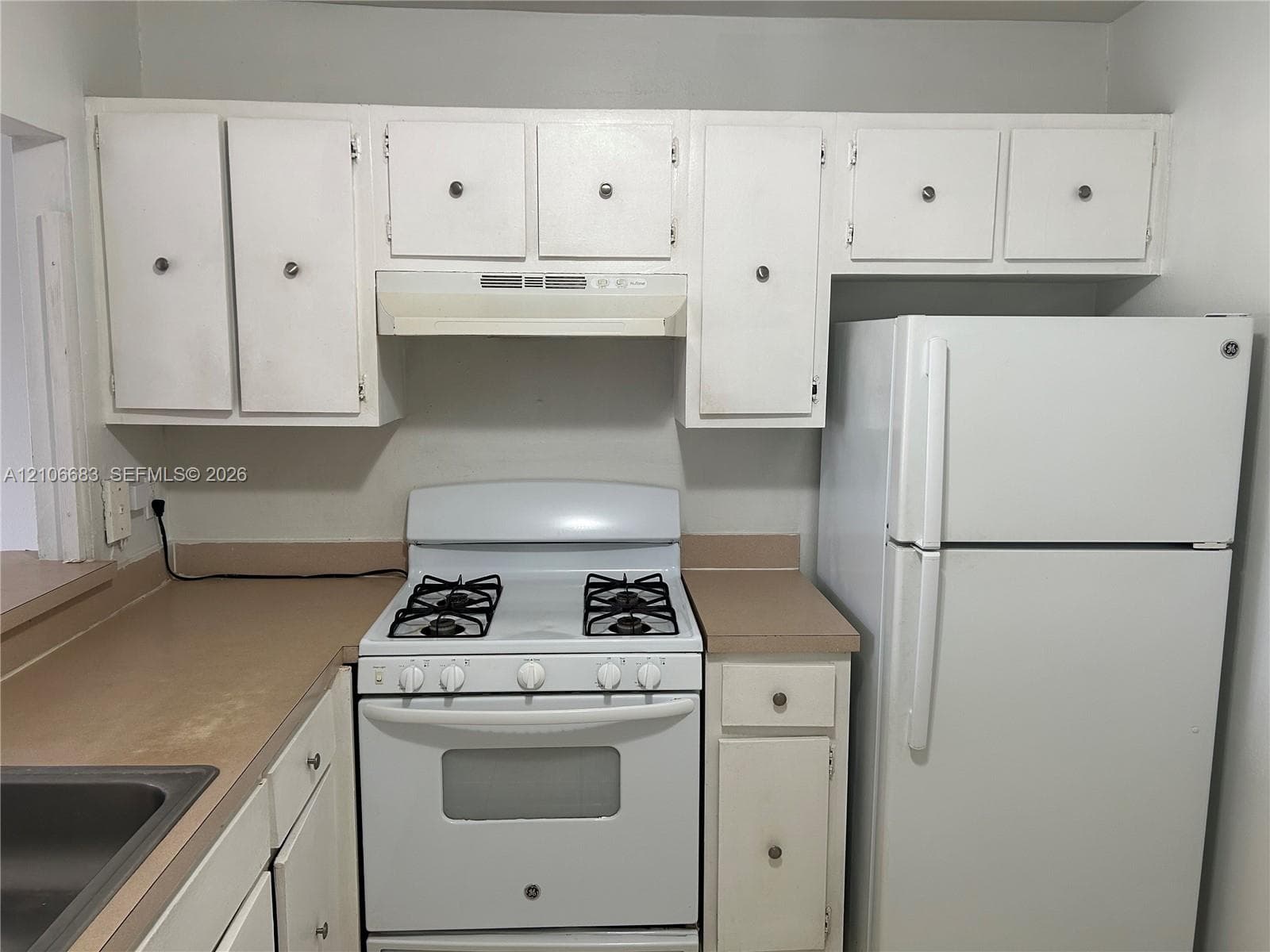 White cabinetry, white gas range, over-the-range exhaust hood, white refrigerator, and solid-surface countertop