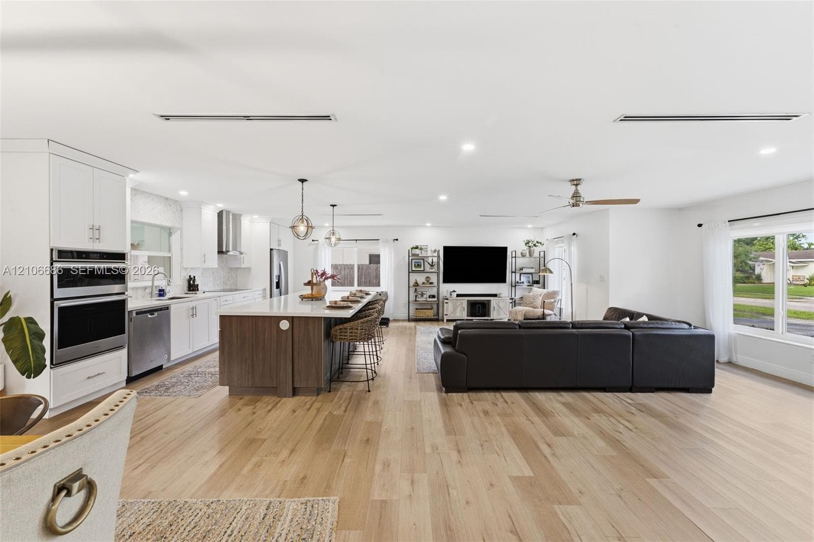 Kitchen featuring a large center island with wood-finish cabinetry, stainless steel appliances including a built-in double oven, quartz countertops, and wood-finish flooring throughout