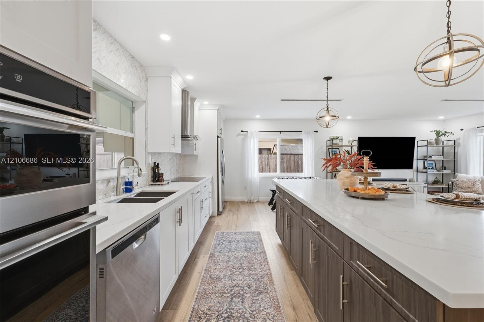 Kitchen featuring an oversized island with a stone countertop, wood-finish cabinetry, stainless steel built-in oven, herringbone tile backsplash, and decorative spherical pendant lighting