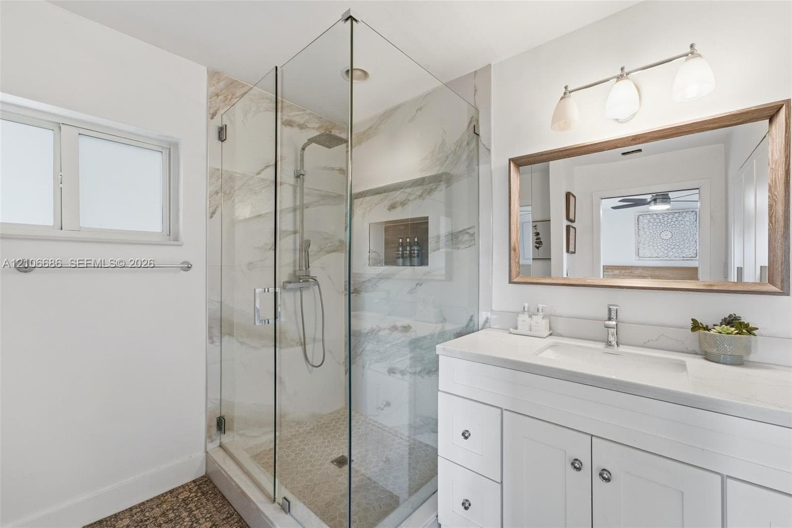 Bathroom featuring a walk-in shower with glass enclosure, large-format stone-patterned tile, integrated wall niche, and rainfall showerhead, complemented by a white vanity with a composite countertop and integrated basin