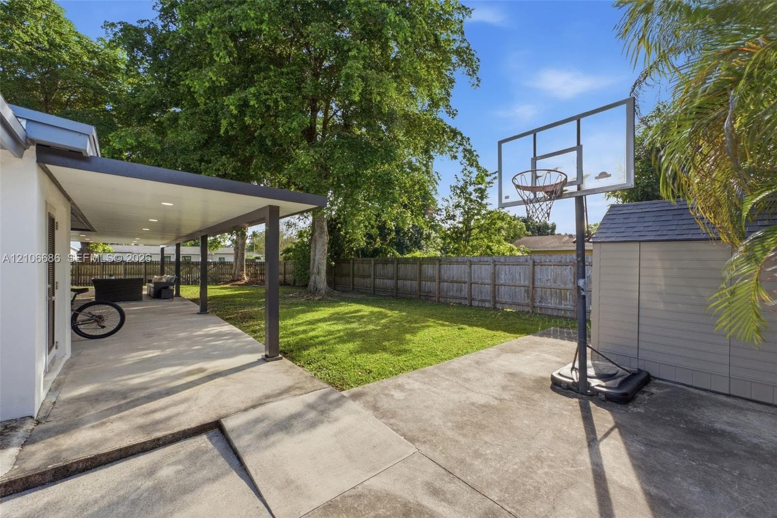 Rear outdoor space featuring a covered concrete patio, level lawn, wood privacy fencing, and exterior storage shed