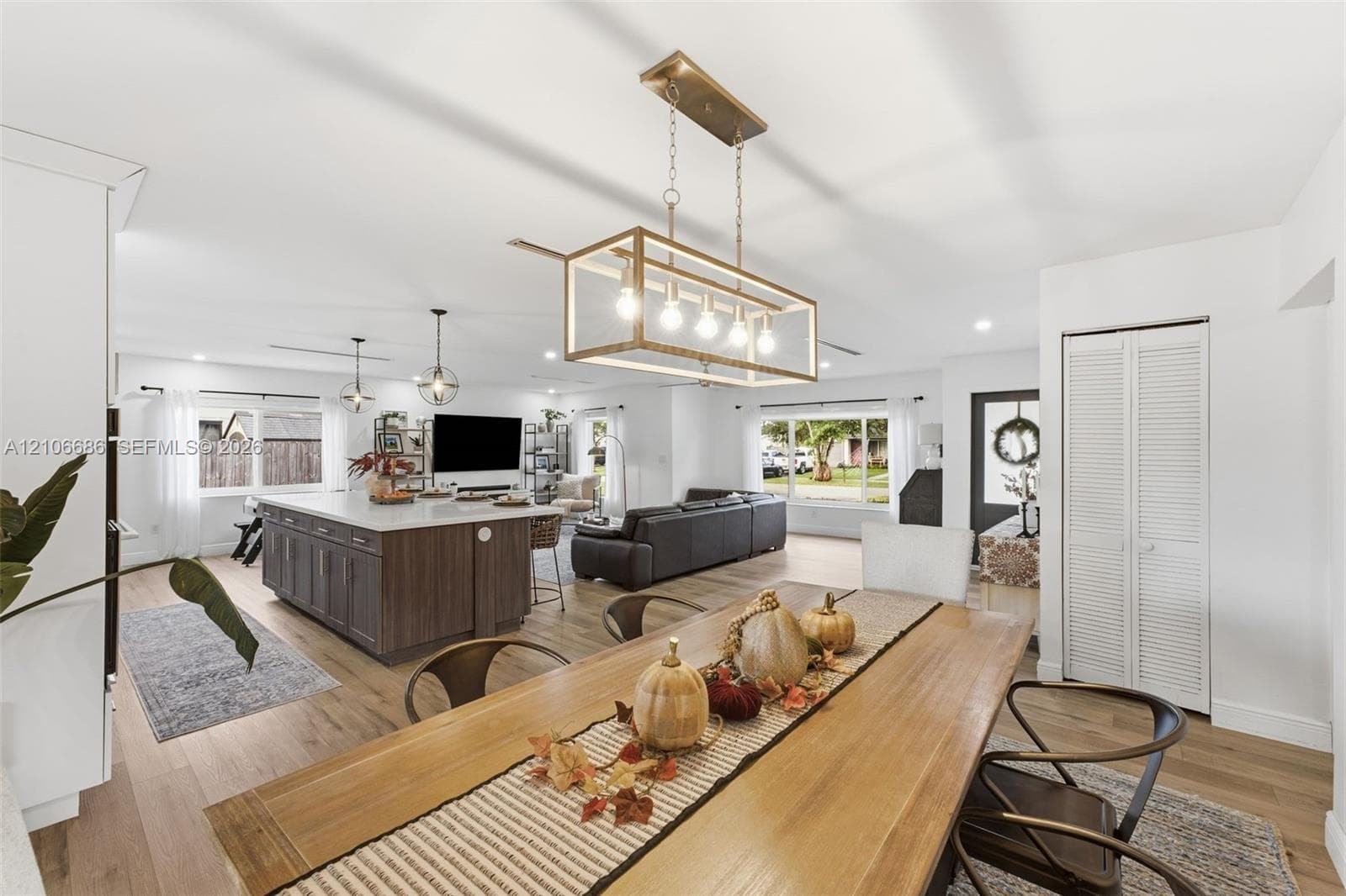 Open-concept area featuring wood-finish flooring, a kitchen island with stone countertop, rectangular linear pendant lighting, and louvered closet doors