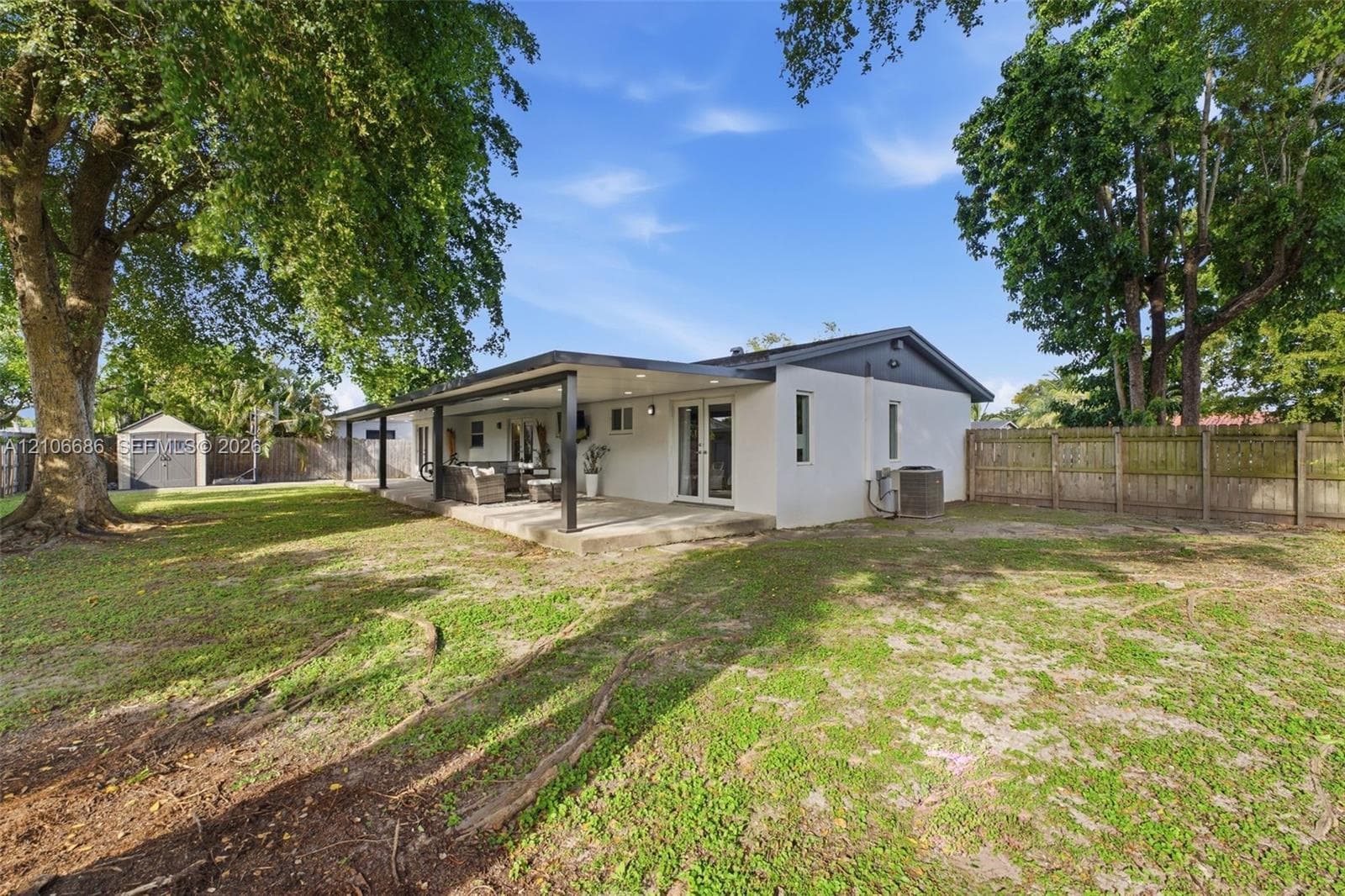 Rear exterior featuring a covered concrete patio, recessed lighting, white stucco siding, dark-trimmed roofline, and a detached storage shed