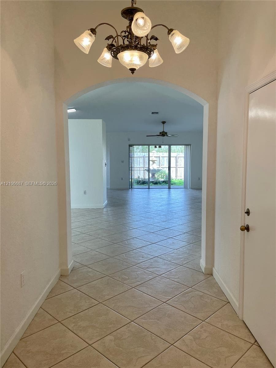 Foyer featuring arched entryway, decorative multi-light chandelier, and ceramic tile flooring extending into the interior space with sliding glass doors