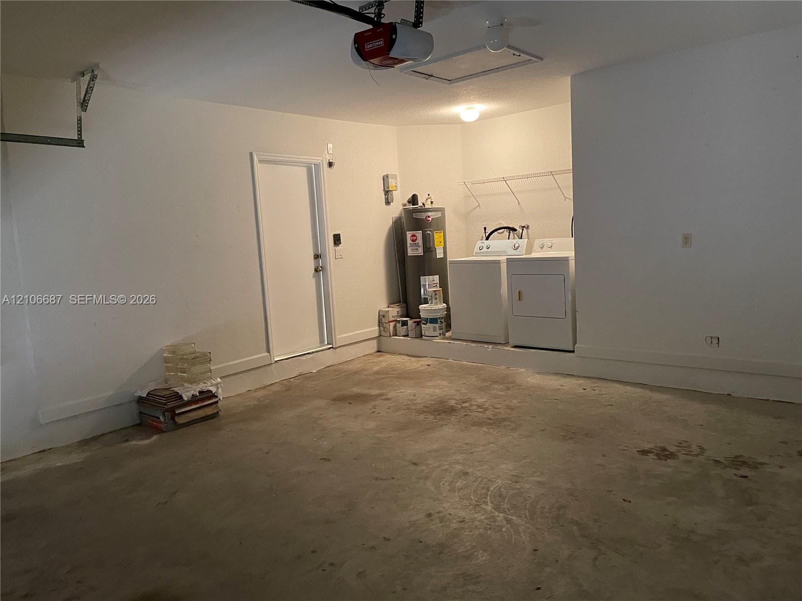 Garage space featuring concrete flooring, an overhead door opener system, a side access door, and a dedicated laundry area with wire shelving