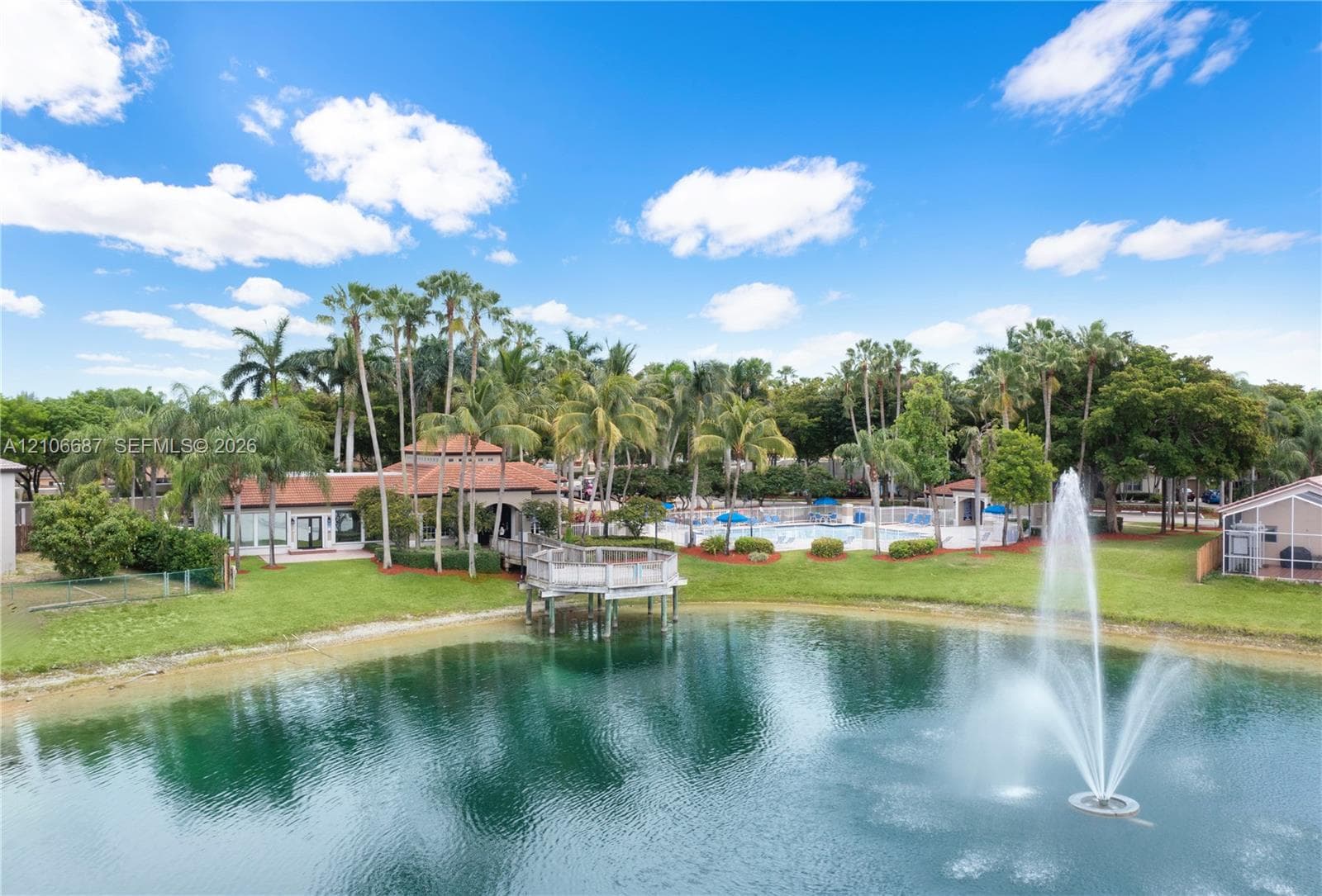 Waterfront property featuring a pond with a fountain, a wooden pier, an outdoor swimming pool, and mature palm trees