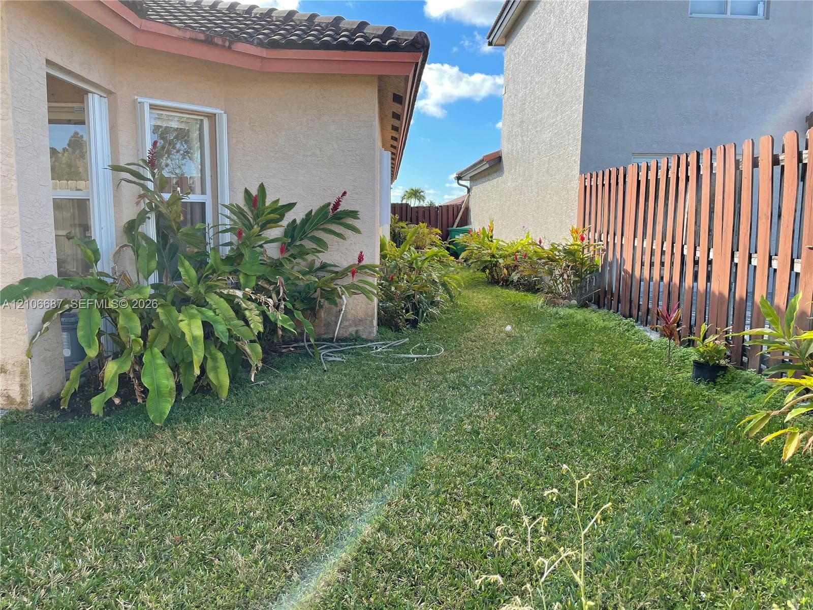 Side yard featuring a manicured lawn, perimeter wood fencing, and established tropical landscaping