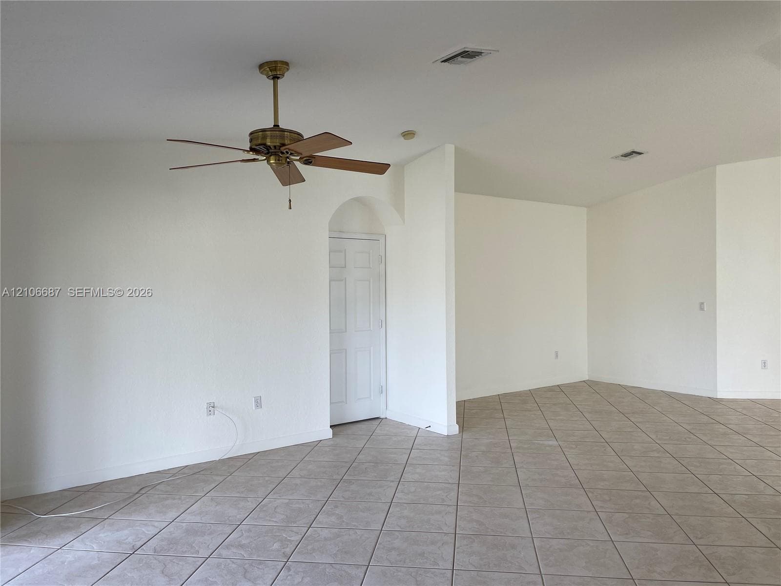 Neutral-toned tile flooring, vaulted ceilings, arched doorway, and multi-speed ceiling fan