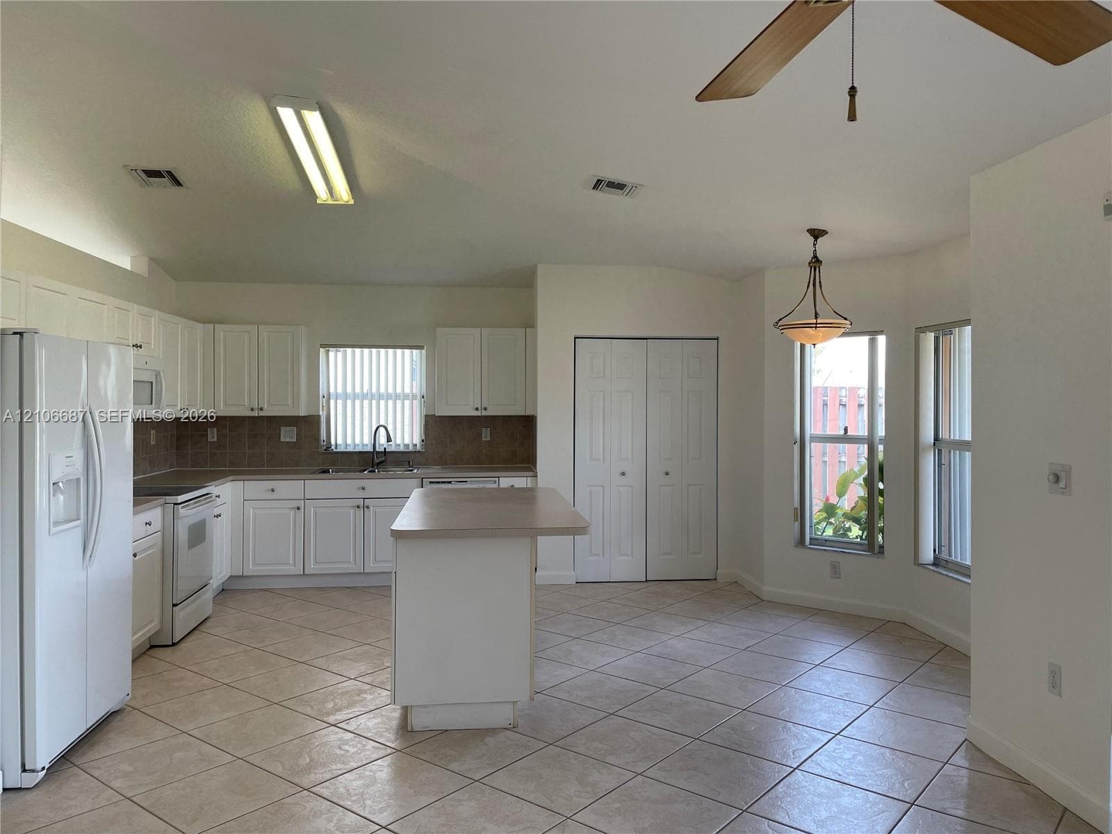 Kitchen featuring white cabinetry, central island with countertop, tile flooring, double-door closet, and pendant lighting
