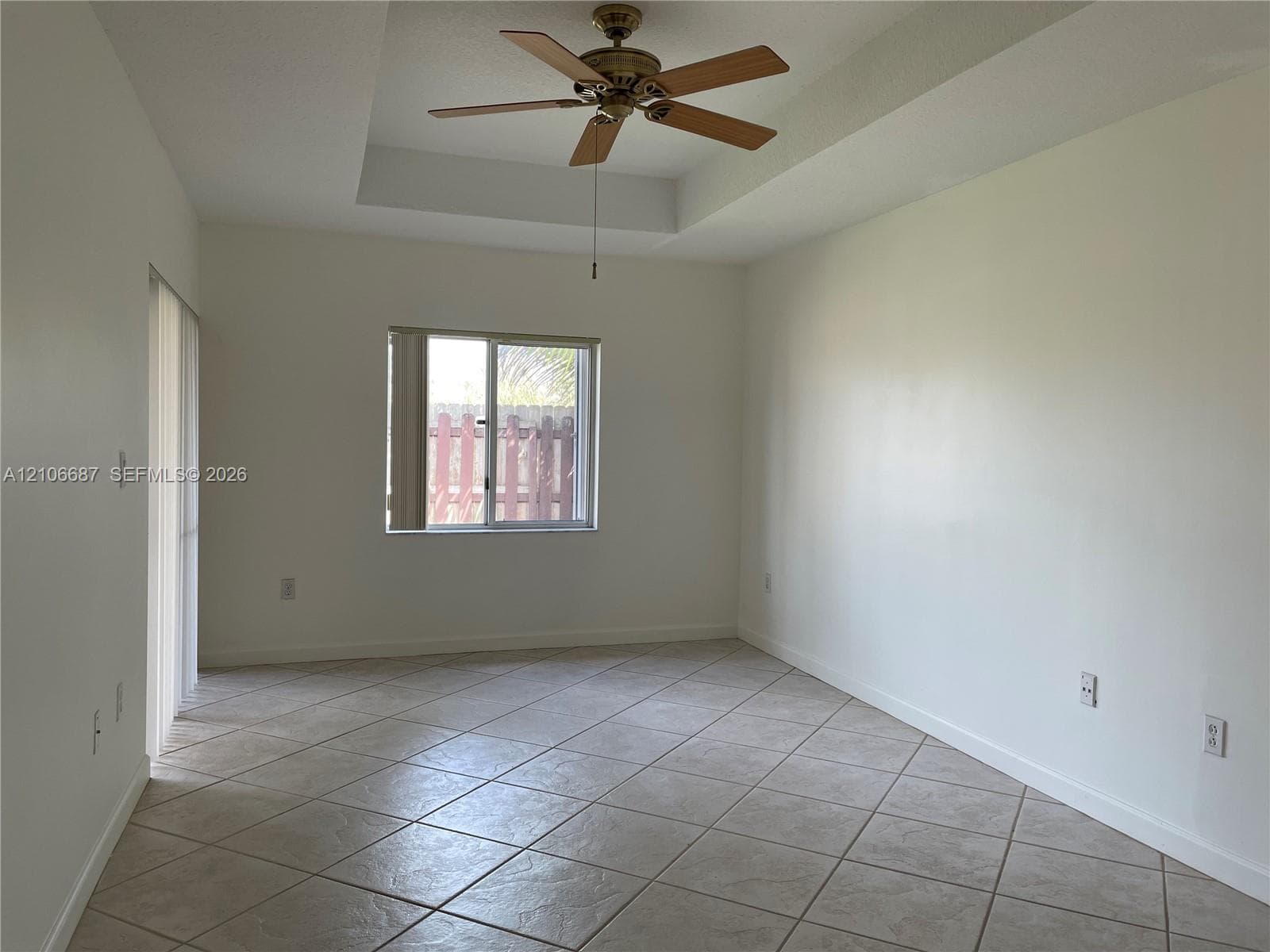Room interior featuring a tray ceiling, ceiling fan with light kit, ceramic tile flooring, and a single-pane window