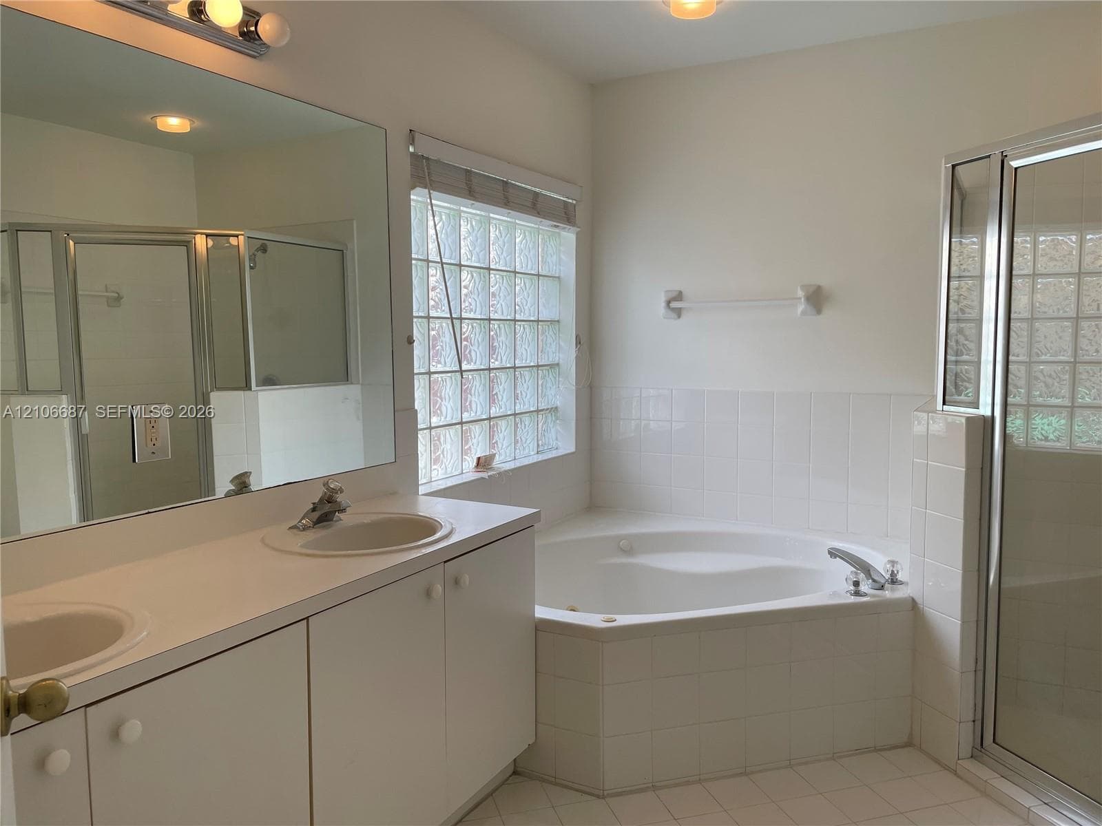 Dual-sink vanity with solid-surface countertop, corner jetted tub, tiled walk-in shower, and glass block window