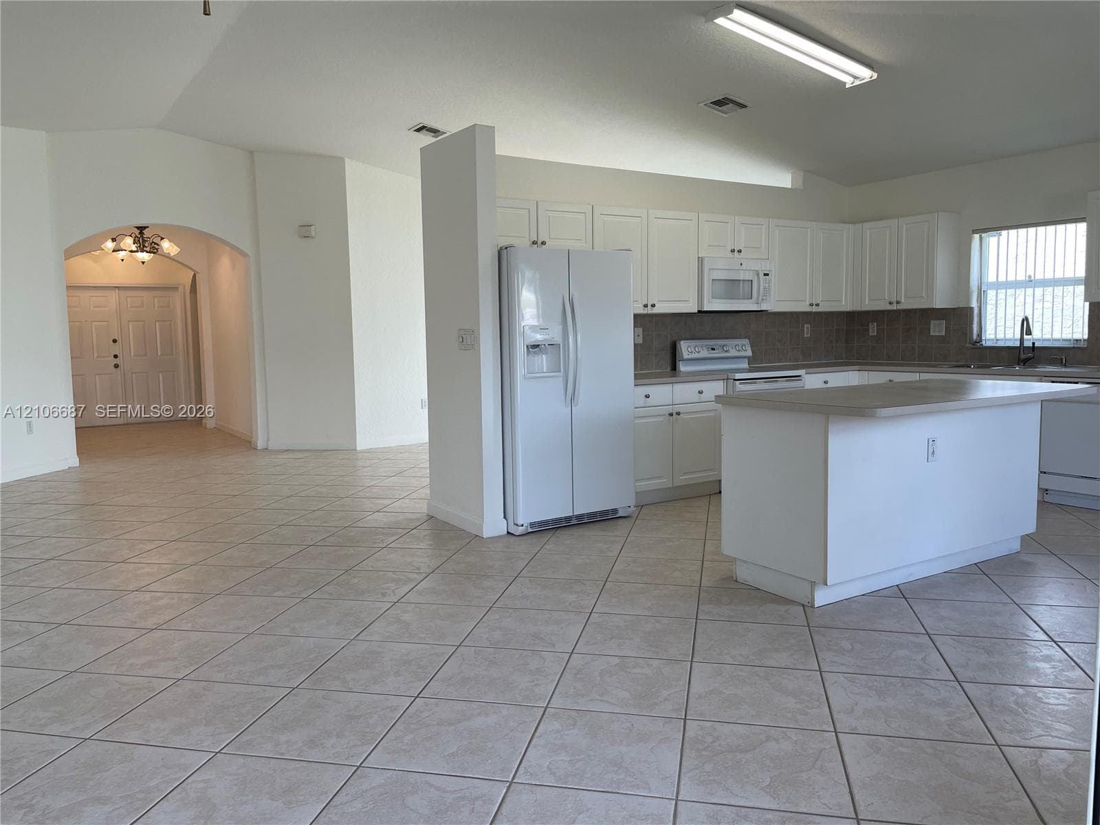 Kitchen featuring white cabinetry, center island, neutral tile flooring, and vaulted ceilings with an arched entryway