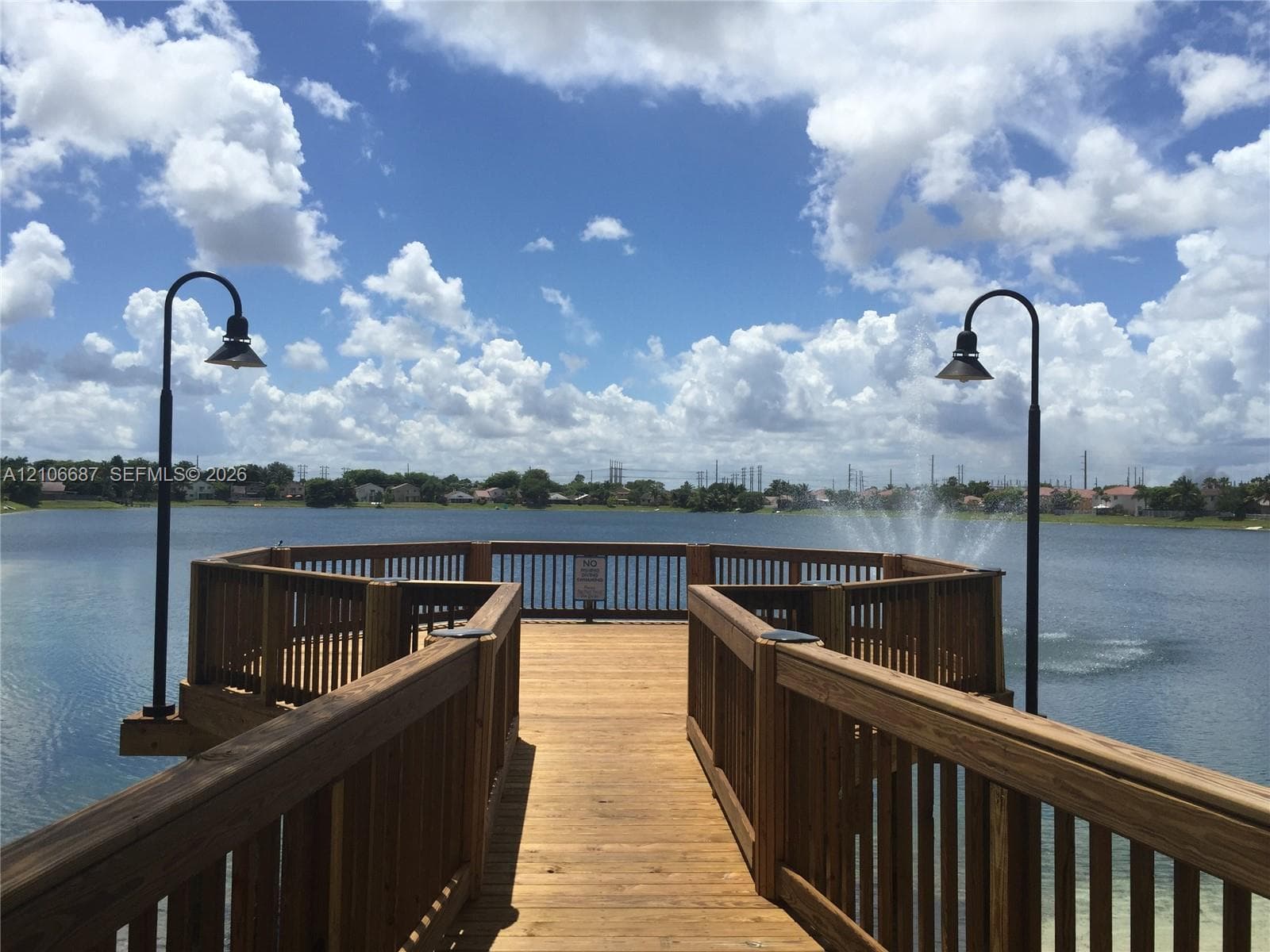 Wooden pier featuring built-in railings, post-mounted lighting, and a platform extending over the water with an integrated fountain