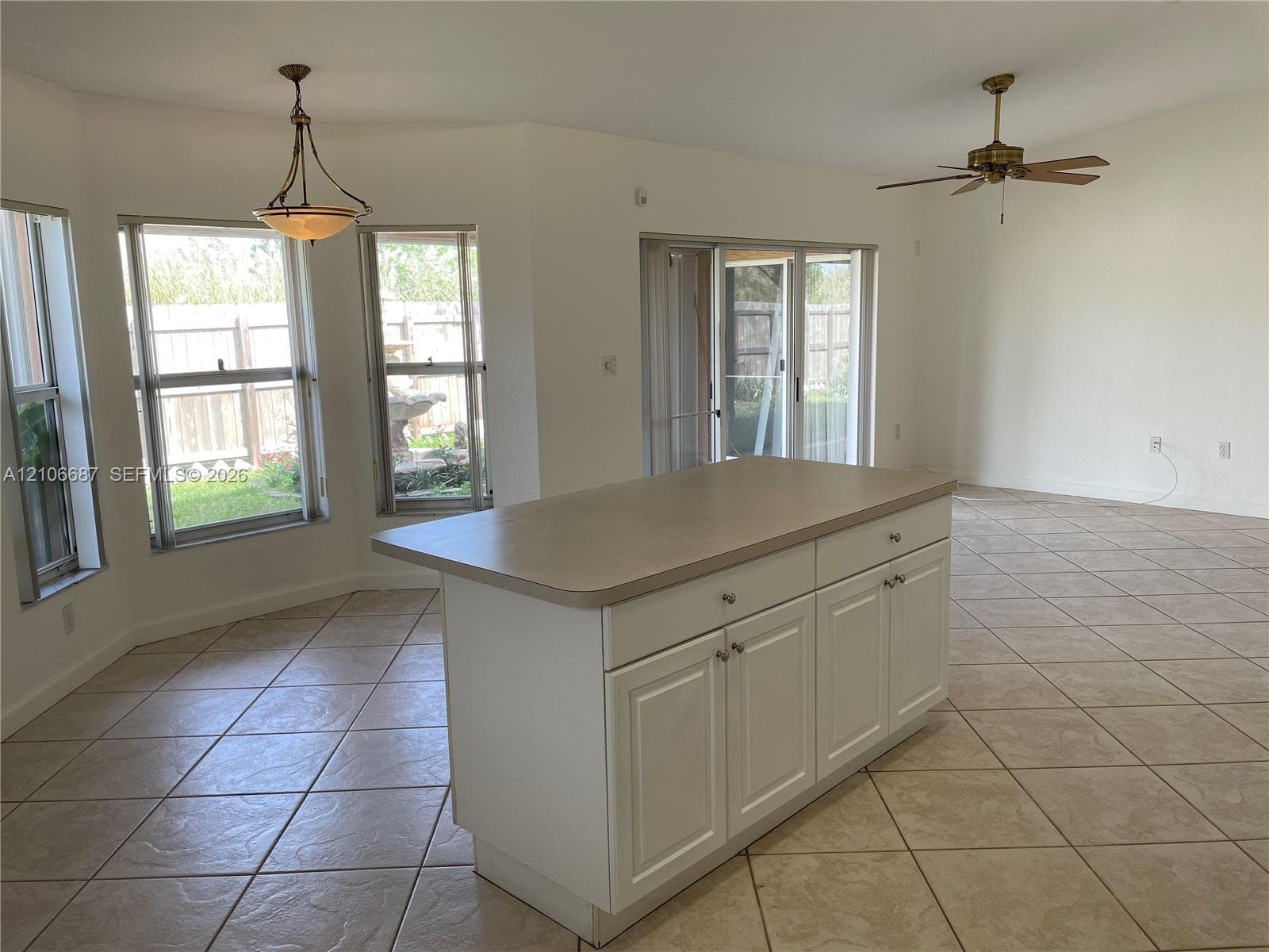 Kitchen featuring a central island with white cabinetry and solid-surface countertop, tile flooring, sliding glass patio doors, and bay-style windows