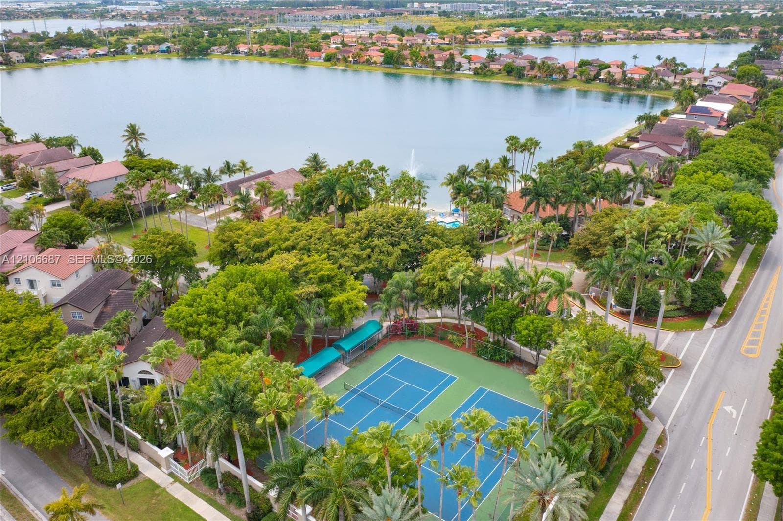 Aerial perspective of dual hard-surface tennis courts featuring perimeter fencing, integrated shade structures, and mature palm tree landscaping