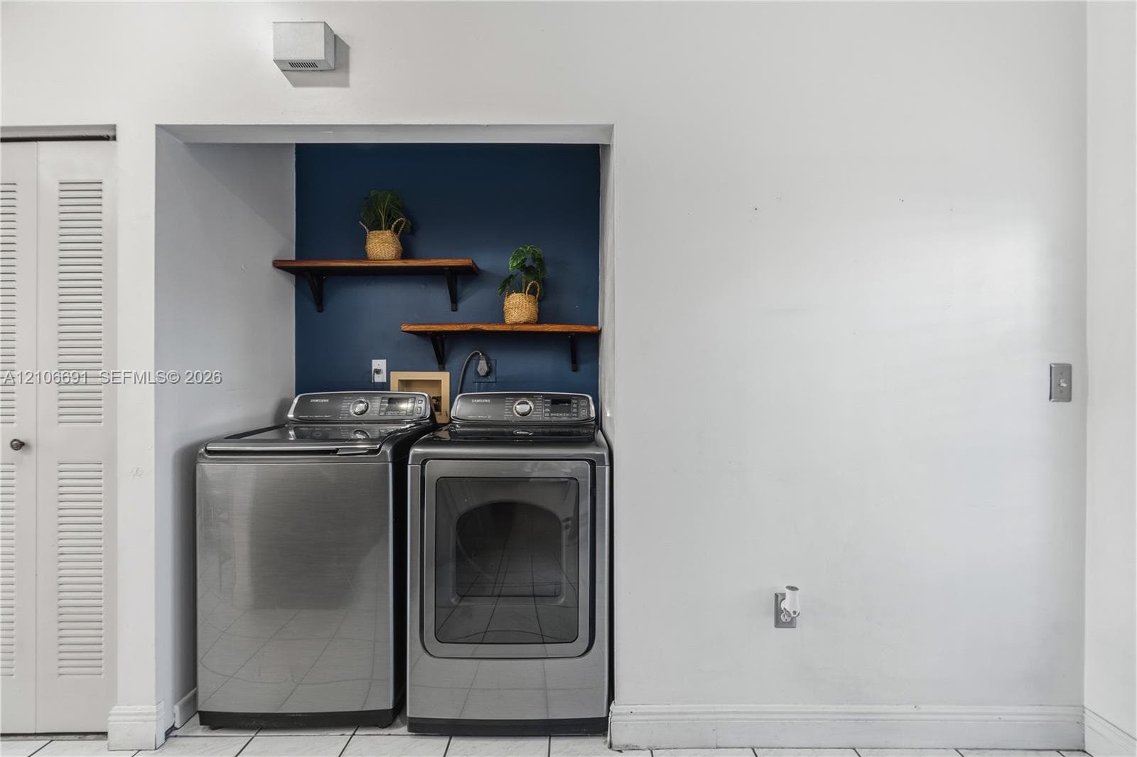 Laundry area featuring stainless steel appliances, dual wall-mounted natural wood shelving, and tiled flooring