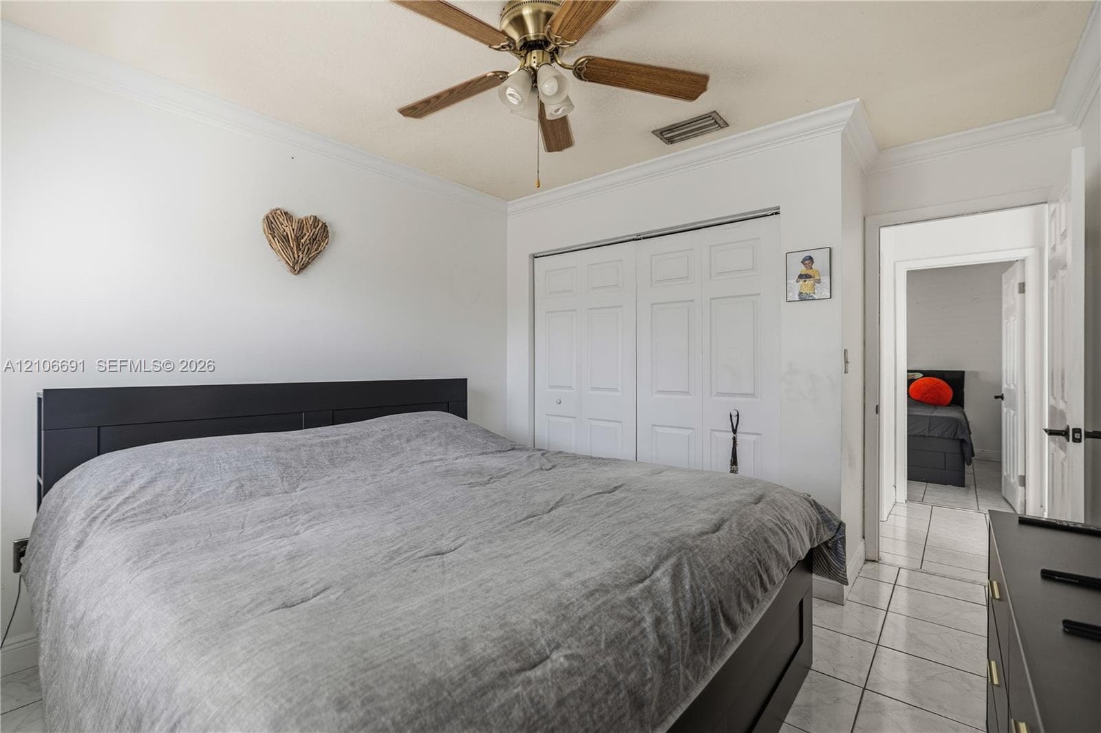 Neutral-toned room featuring crown molding, ceramic tile flooring, a dual-paneled closet, and a multi-blade ceiling fan with integrated lighting