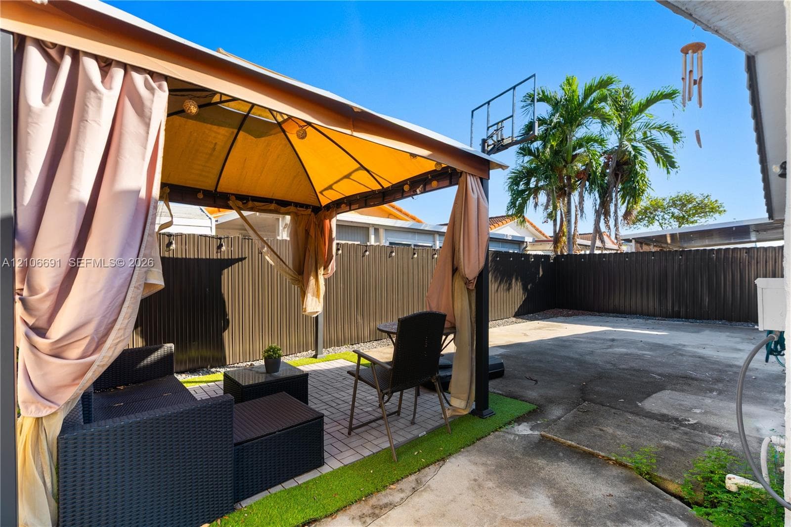Backyard featuring a metal-frame gazebo, paved patio area, tall metal privacy fencing, and a built-in basketball hoop