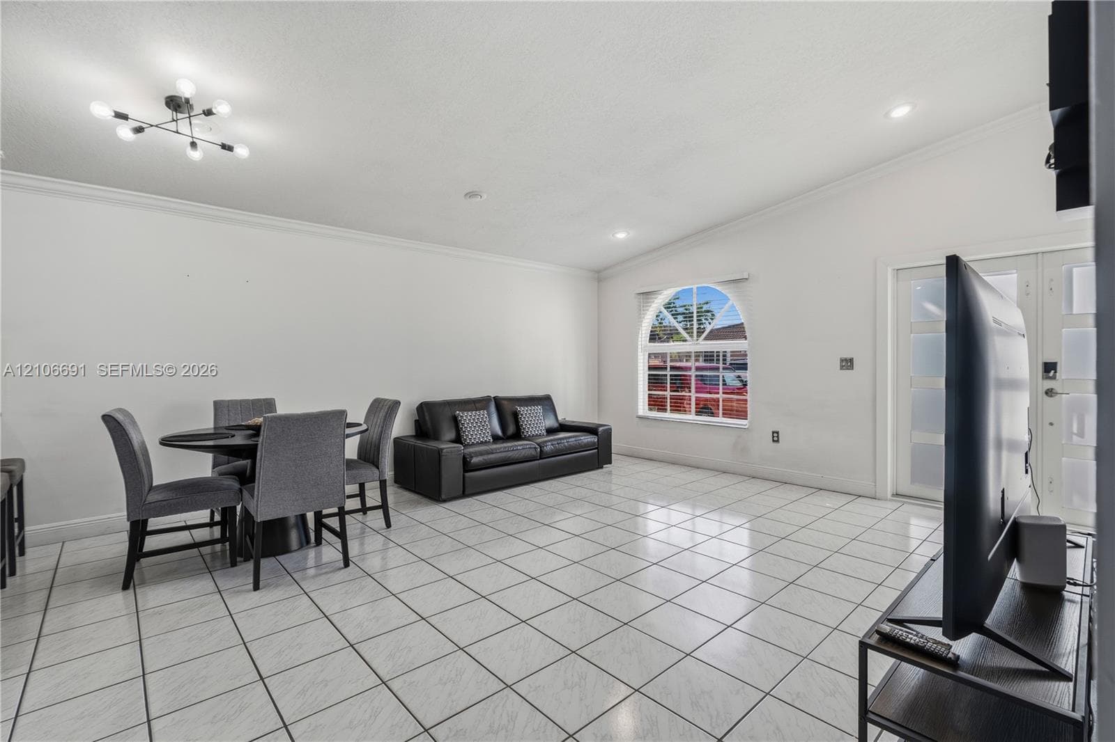 Open-concept interior featuring light-toned tile flooring, vaulted ceilings, a prominent arched window, recessed lighting, and a multi-light chandelier