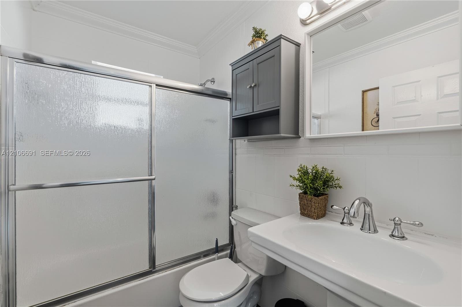 Wall-mounted charcoal cabinetry, pedestal sink with chrome dual-handle faucet, white subway tile walls, and a glass-enclosed shower featuring a sliding door