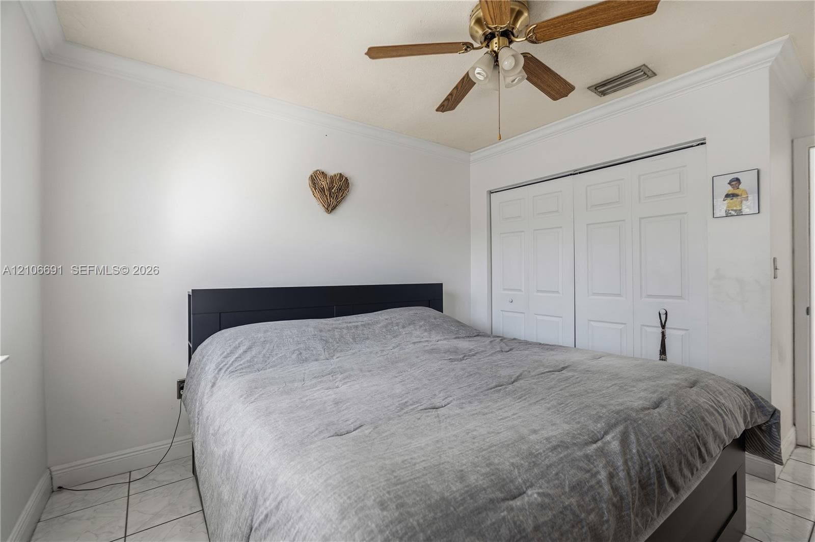 Room featuring neutral wall finishes, tile flooring, crown molding, double-panel sliding closet doors, and a ceiling fan with integrated lighting