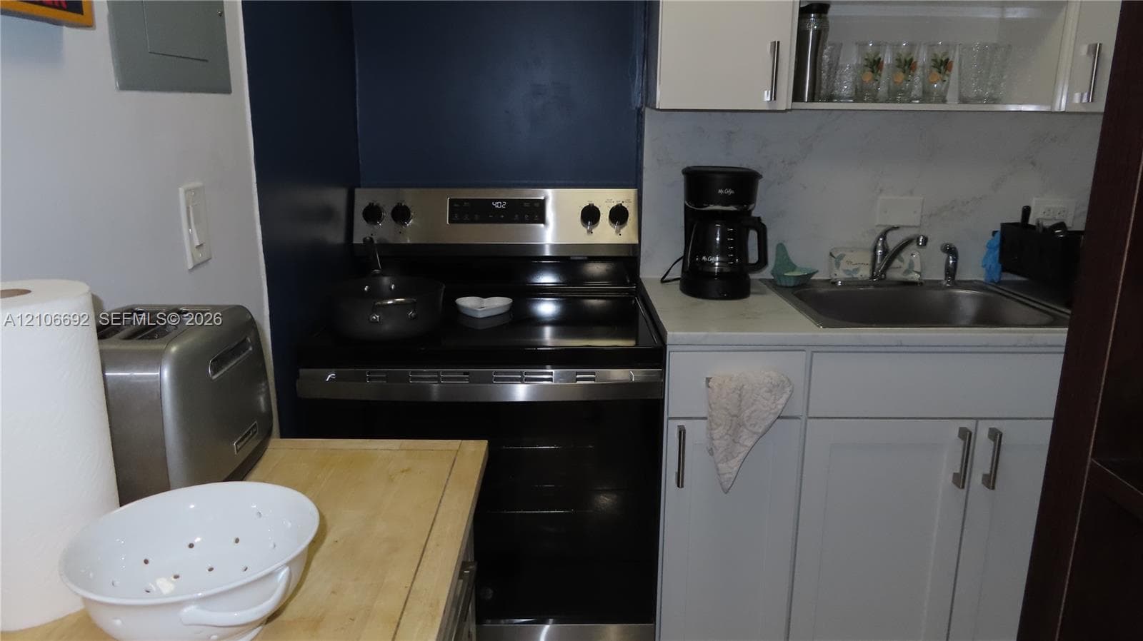 Stainless steel electric range, light gray cabinetry, stone-finish countertops, undermount sink, and integrated open shelving